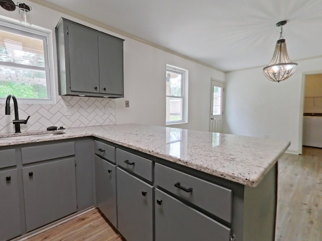 kitchen with decorative backsplash, a peninsula, light wood-style floors, a sink, and gray cabinetry