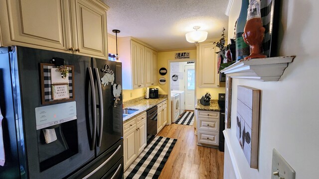 kitchen featuring black appliances, cream cabinets, light wood-style flooring, and independent washer and dryer