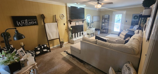 carpeted living room featuring a brick fireplace, ornamental molding, ceiling fan, and wood walls