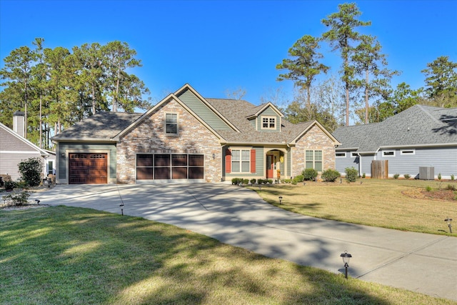 traditional-style home featuring central AC unit, stone siding, concrete driveway, a shingled roof, and a front yard