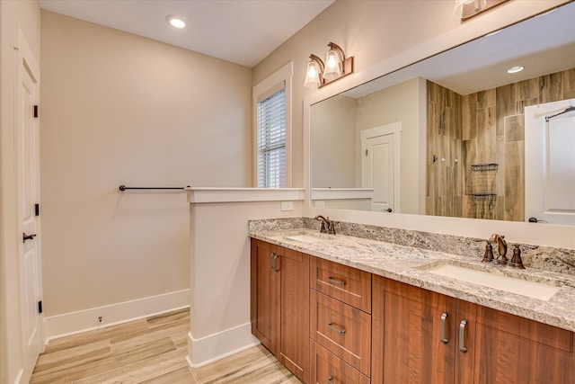 bathroom with a tile shower, wood finished floors, baseboards, and a sink