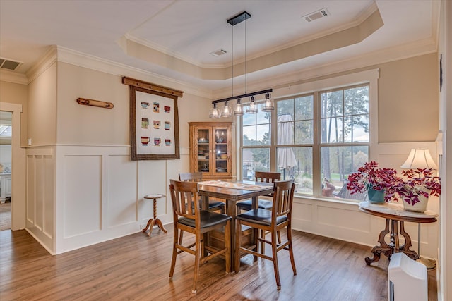 dining space featuring a tray ceiling, wood finished floors, visible vents, and a decorative wall