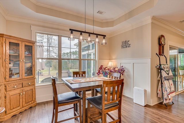 dining space featuring a tray ceiling, a decorative wall, light wood-style flooring, and visible vents