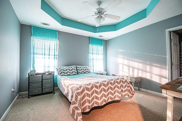 bedroom featuring a ceiling fan, a tray ceiling, visible vents, and baseboards