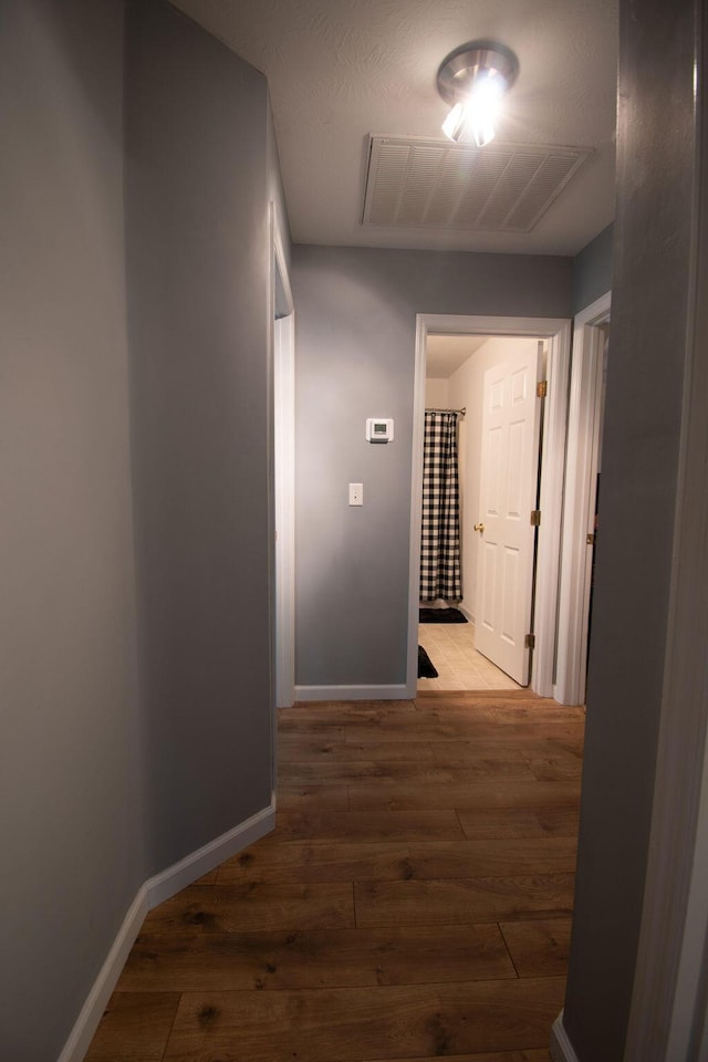 hall featuring baseboards, visible vents, and hardwood / wood-style floors