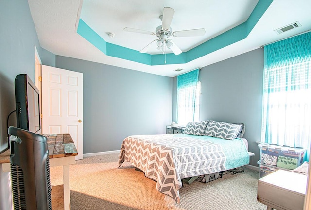 bedroom with a tray ceiling, carpet, visible vents, and baseboards