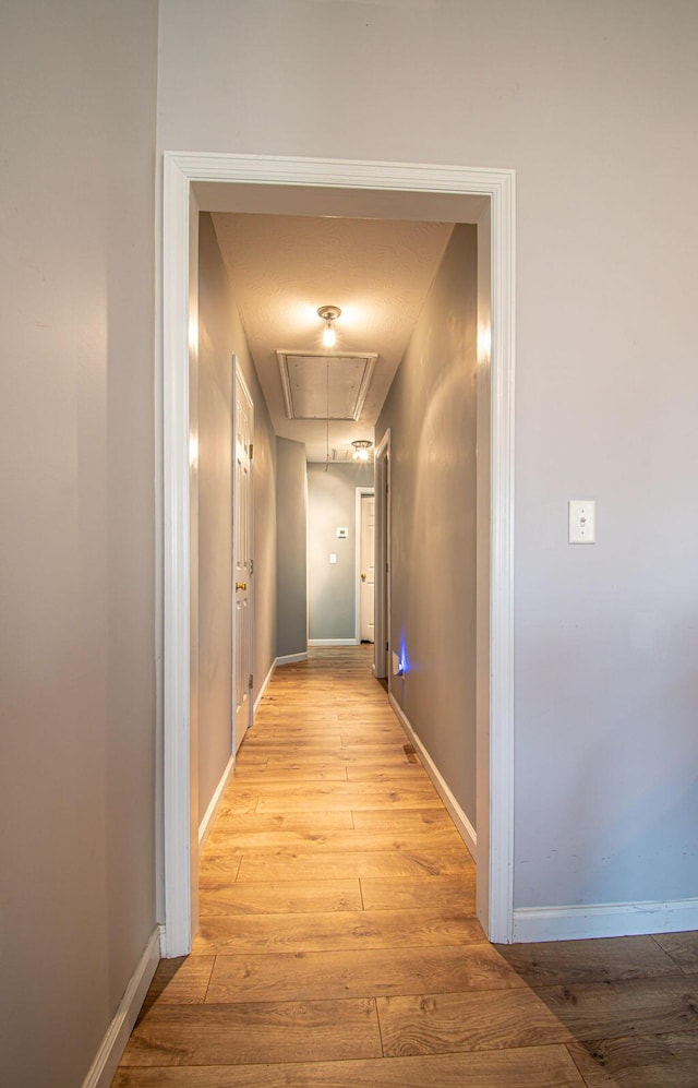 corridor featuring light wood finished floors, attic access, and baseboards