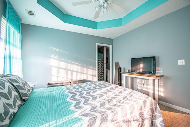 carpeted bedroom with a ceiling fan, a tray ceiling, visible vents, and baseboards