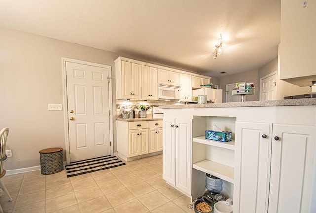 kitchen with light tile patterned floors, decorative backsplash, white microwave, light countertops, and open shelves