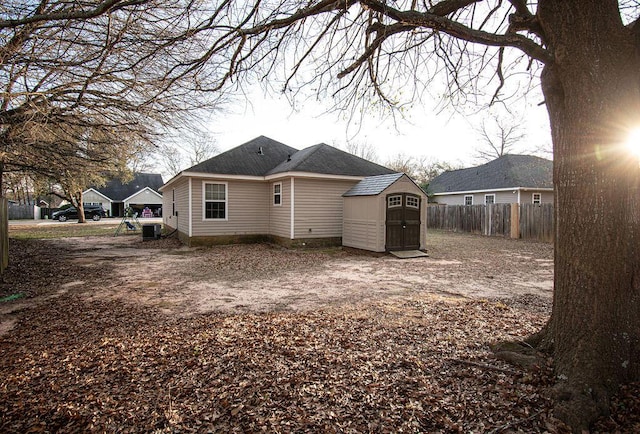 rear view of property featuring a shingled roof, fence, a storage unit, and an outdoor structure