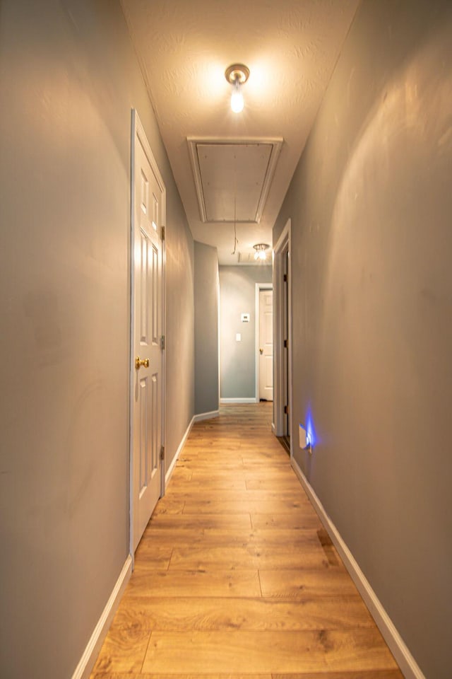 hall with light wood-style floors, attic access, and baseboards