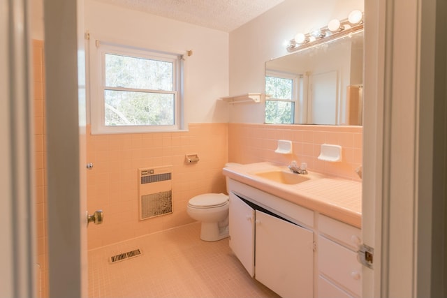 bathroom with tile patterned floors, vanity, heating unit, tile walls, and plenty of natural light