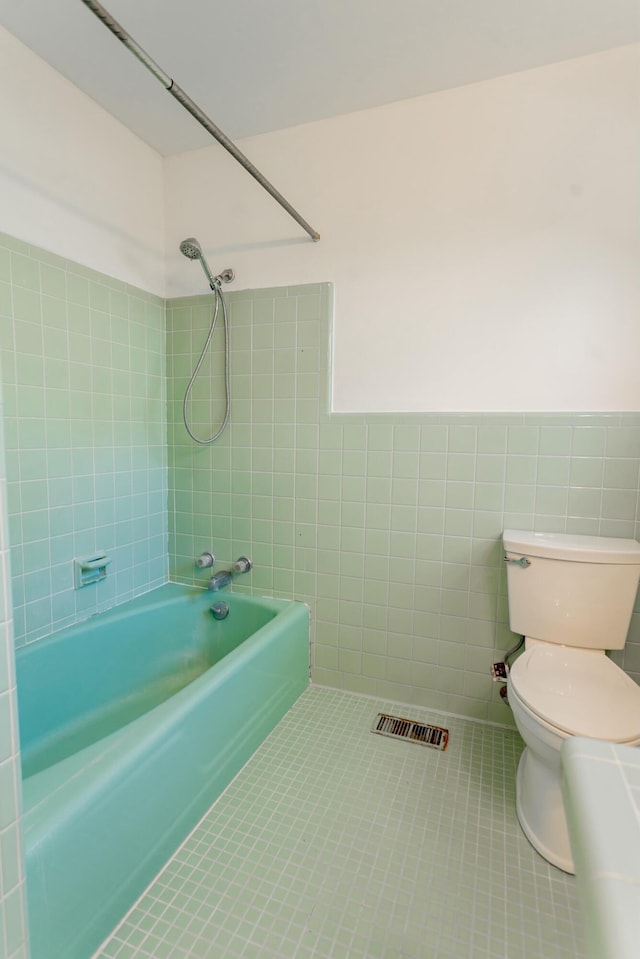 bathroom with toilet, tile patterned flooring, tile walls, and tiled shower / bath