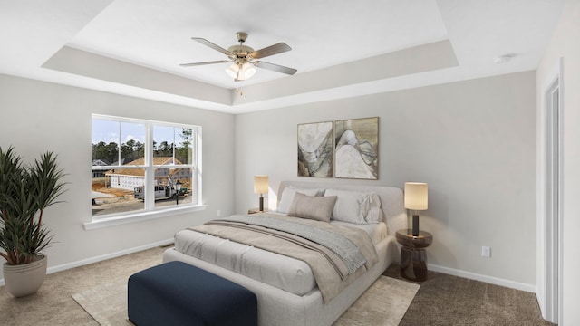 bedroom with a tray ceiling, light colored carpet, and baseboards
