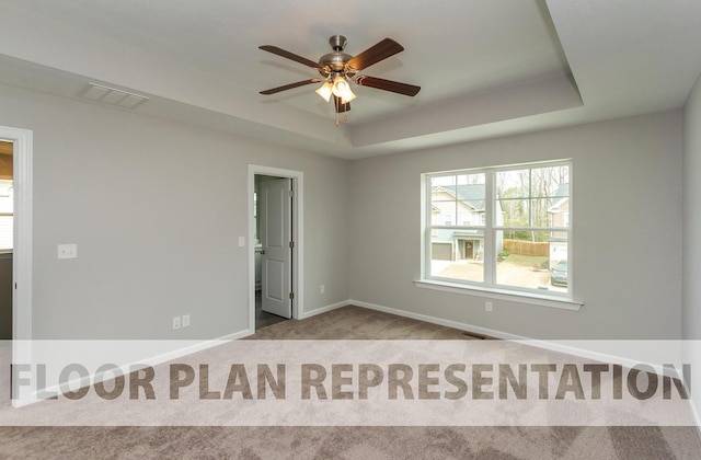 empty room with a tray ceiling, carpet flooring, visible vents, and baseboards