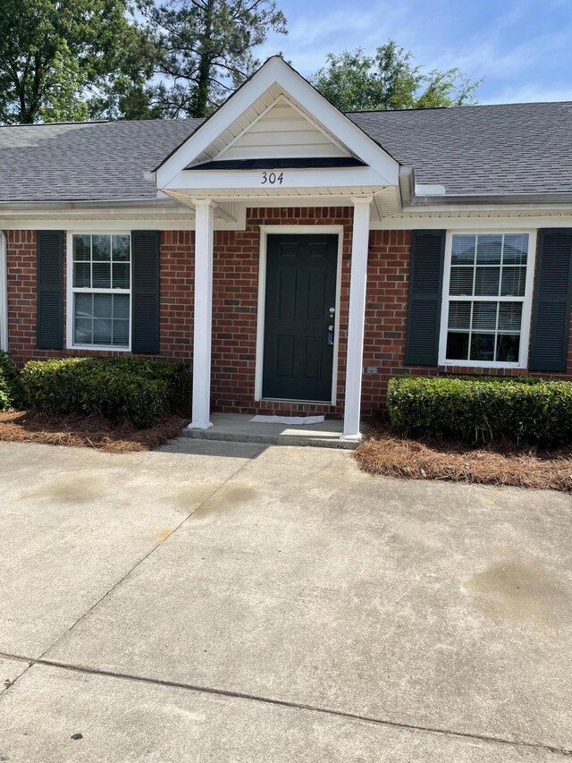 property entrance featuring a shingled roof and brick siding