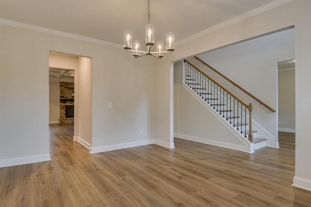 unfurnished dining area featuring baseboards, stairway, ornamental molding, wood finished floors, and a notable chandelier