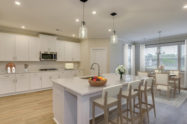 kitchen featuring stainless steel microwave, light wood-style flooring, ornamental molding, and a sink