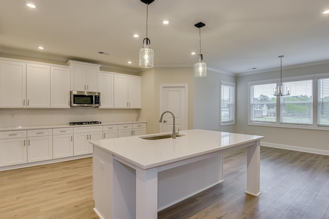 kitchen with ornamental molding, a sink, stainless steel microwave, light wood-style floors, and white cabinets