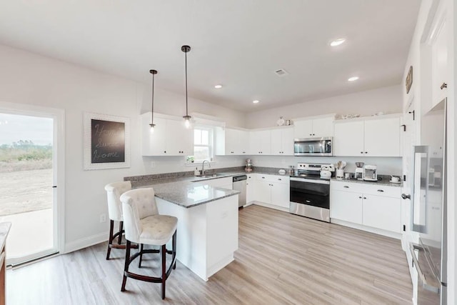 kitchen with a healthy amount of sunlight, hanging light fixtures, white cabinets, appliances with stainless steel finishes, and a kitchen breakfast bar