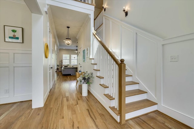 stairs with ornamental molding, a decorative wall, and wood finished floors