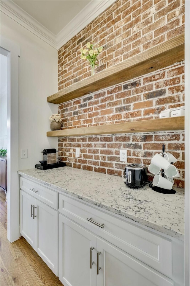 bar featuring light wood-type flooring, brick wall, and crown molding