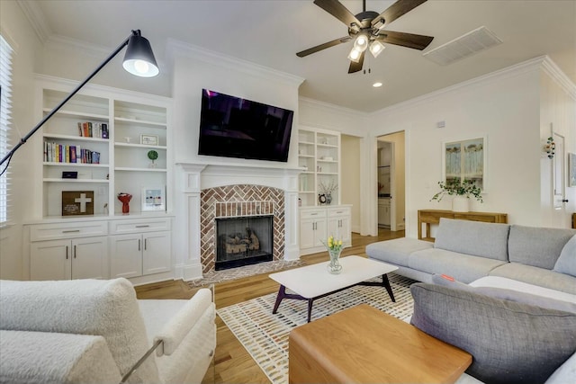 living room with light wood-type flooring, visible vents, a tiled fireplace, and ornamental molding