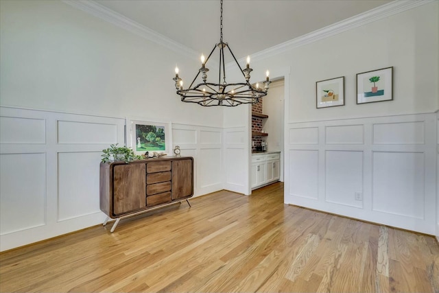 dining space with light wood-style flooring, ornamental molding, and a decorative wall