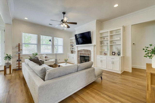 living room with ornamental molding, a fireplace, light wood finished floors, and a ceiling fan