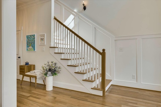 staircase with crown molding, a decorative wall, and wood finished floors