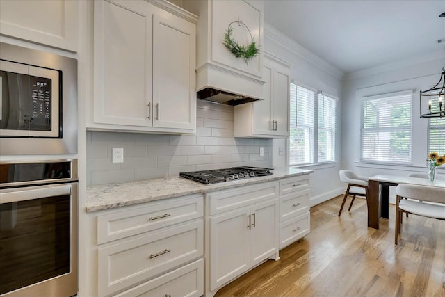 kitchen with light wood finished floors, stainless steel appliances, decorative backsplash, ornamental molding, and white cabinets