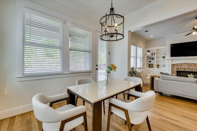 dining room featuring built in shelves, a fireplace, wood finished floors, baseboards, and crown molding