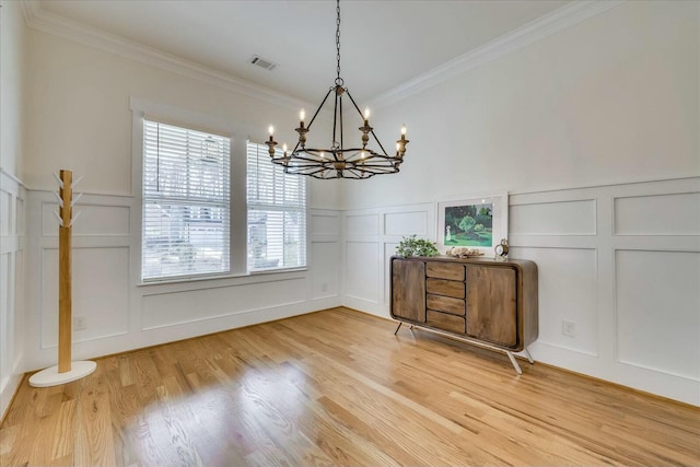 unfurnished dining area featuring a decorative wall, visible vents, wainscoting, light wood-type flooring, and crown molding