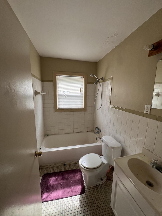 bathroom with toilet, tile patterned floors,  shower combination, vanity, and tile walls