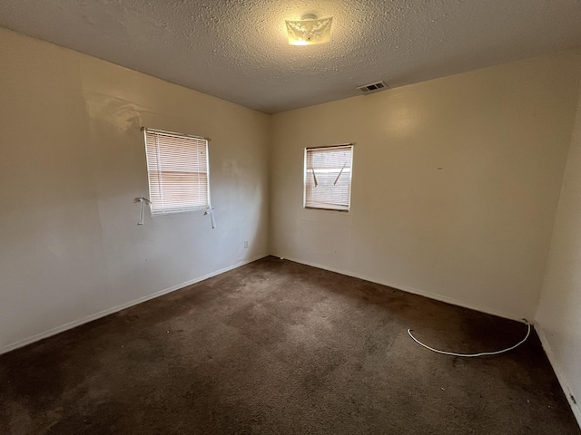 spare room featuring visible vents, dark carpet, and a textured ceiling