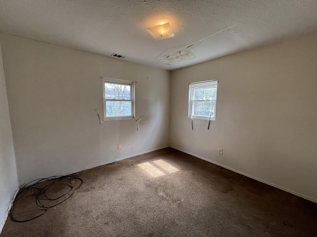 unfurnished room featuring a textured ceiling, dark colored carpet, visible vents, and a healthy amount of sunlight