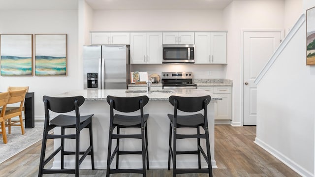 kitchen featuring white cabinetry, a center island with sink, appliances with stainless steel finishes, and light stone counters