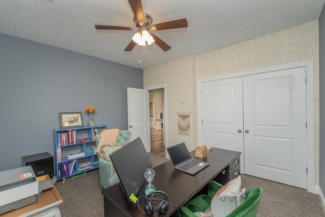 carpeted home office with baseboards, a textured ceiling, ceiling fan, and wallpapered walls