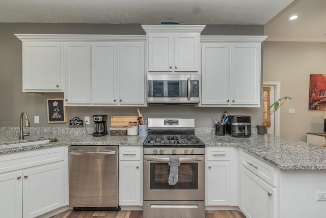 kitchen featuring a sink, a peninsula, stainless steel appliances, recessed lighting, and white cabinetry