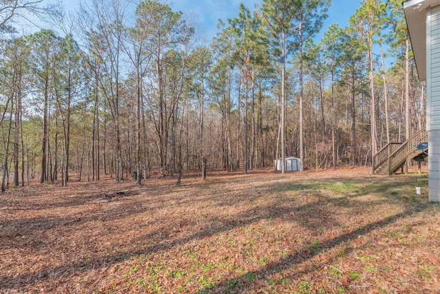 view of yard with an outdoor structure, a storage shed, stairway, and a forest view