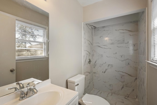 bathroom featuring toilet, tiled shower, and vanity