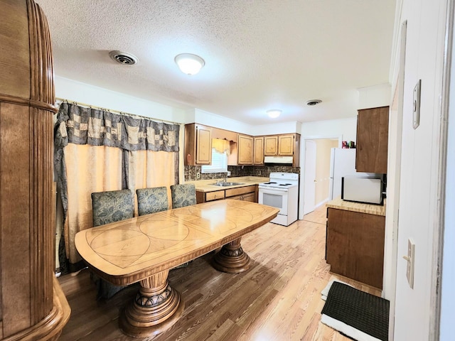 kitchen featuring decorative backsplash, white appliances, a textured ceiling, and light hardwood / wood-style flooring