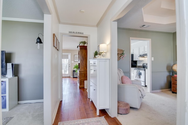 hallway with visible vents, crown molding, light wood-style flooring, and baseboards