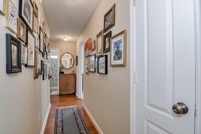 corridor featuring a textured ceiling, baseboards, and wood finished floors