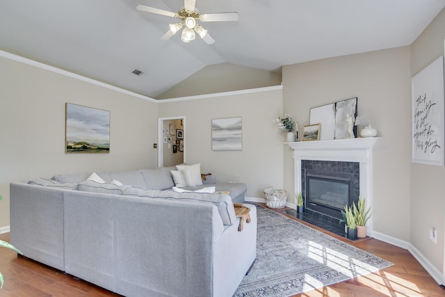 living room with lofted ceiling, visible vents, a tiled fireplace, a ceiling fan, and wood finished floors