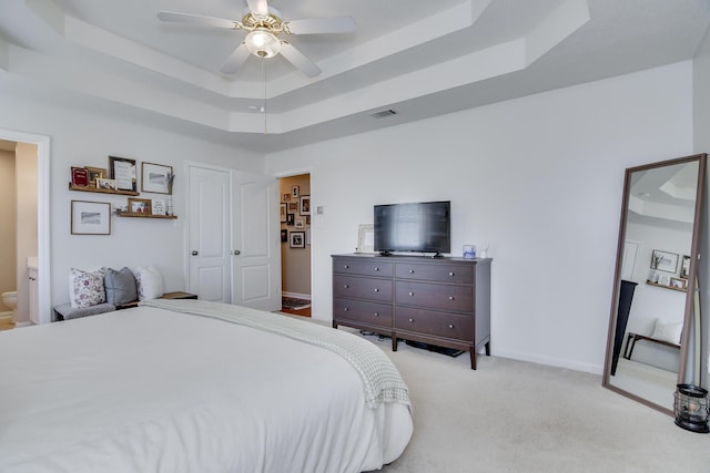 bedroom featuring light carpet, a tray ceiling, visible vents, and baseboards