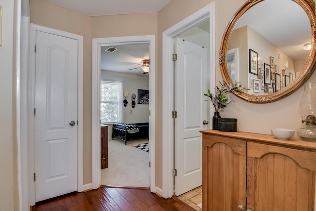 hallway with dark wood-style floors, visible vents, and baseboards