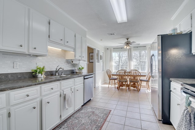 kitchen with light tile patterned floors, a sink, white cabinets, appliances with stainless steel finishes, and dark countertops