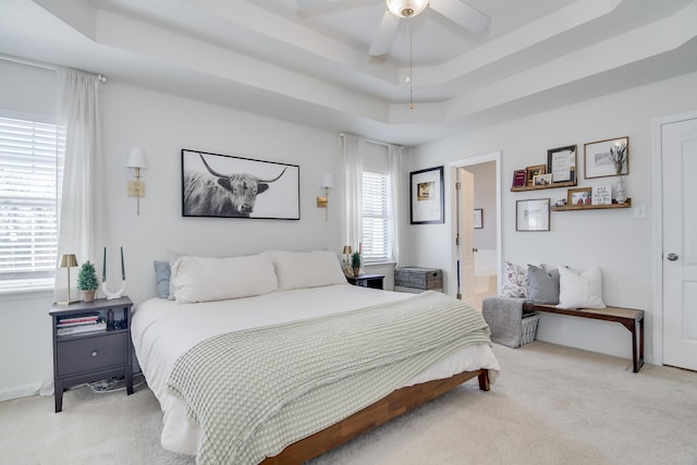 bedroom with ceiling fan, a raised ceiling, and light colored carpet