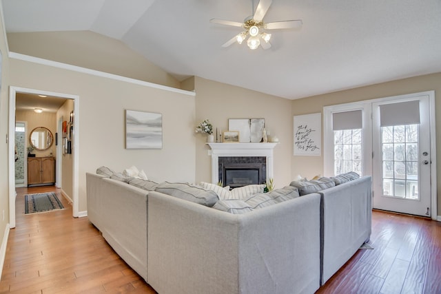 living room featuring vaulted ceiling, a premium fireplace, wood finished floors, and a ceiling fan